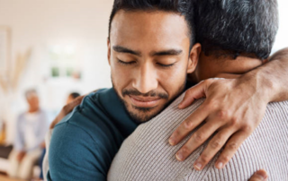 Two people embrace one another in a support group meeting.