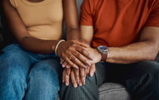 Two people sitting on a couch, one is being comforted by the other.